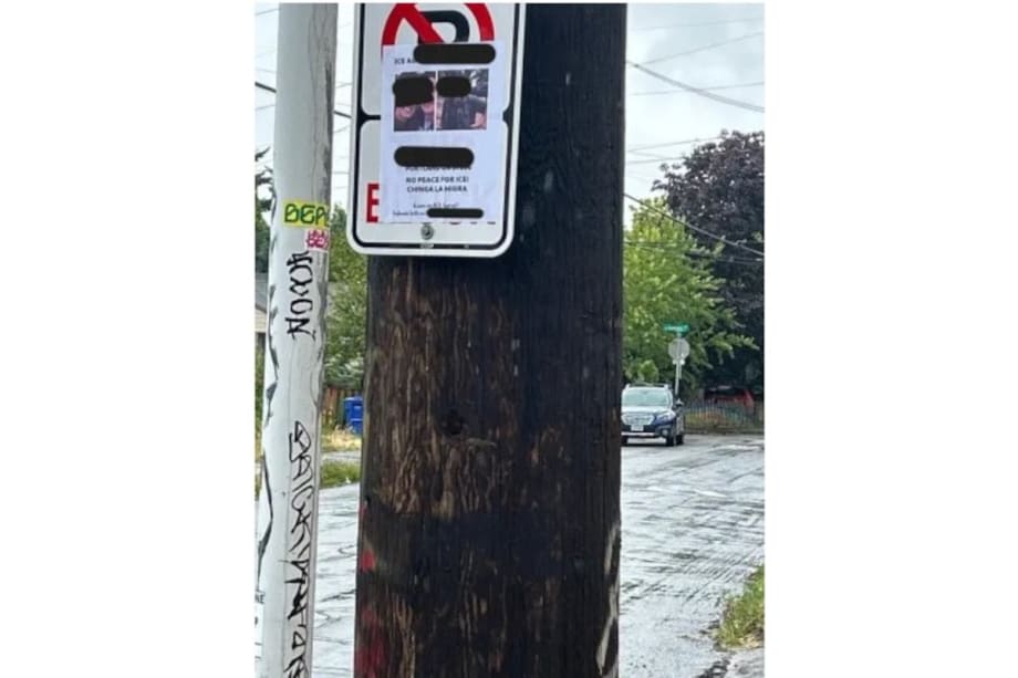 Wooden utility pole with street sign, wet pavement, and trees in background