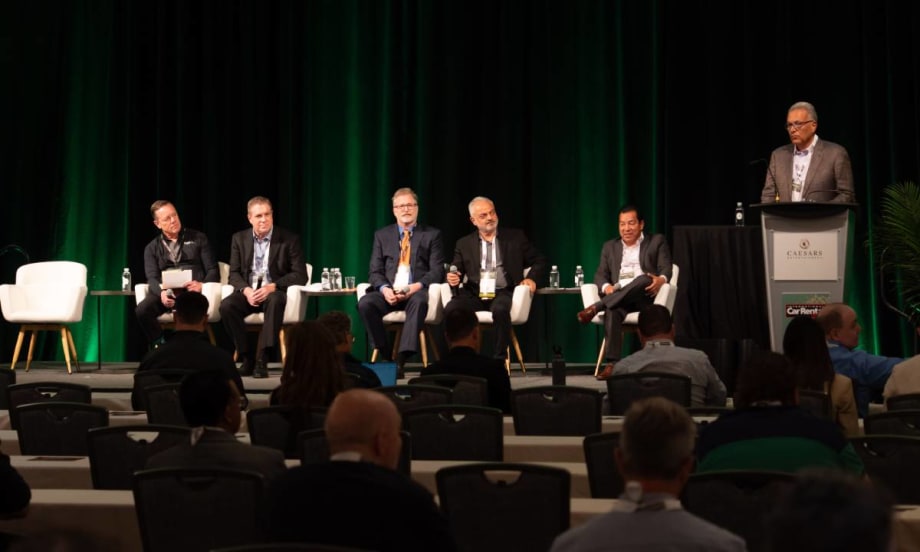 Five panelists sitting in white chairs and a moderator at the podium on stage at ICRS