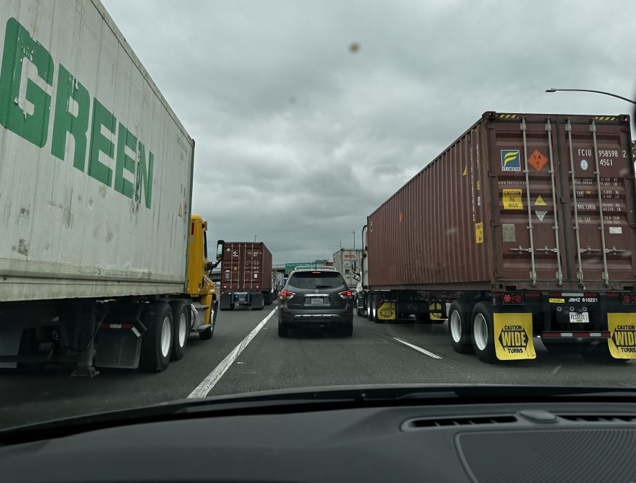 A passenger car stuck in traffic on highway next to big rigs.