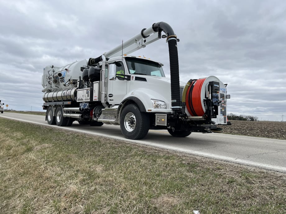 A white Vactor 2100i is seen on the side of the road, with the new longer hose positioned up front.