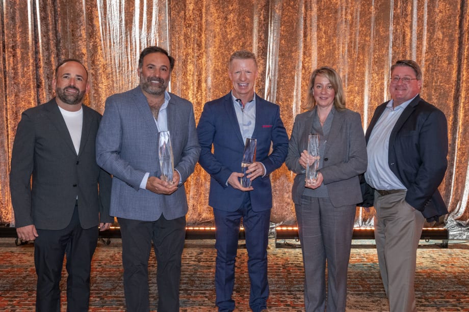 Five people stand against a gold background holding awards