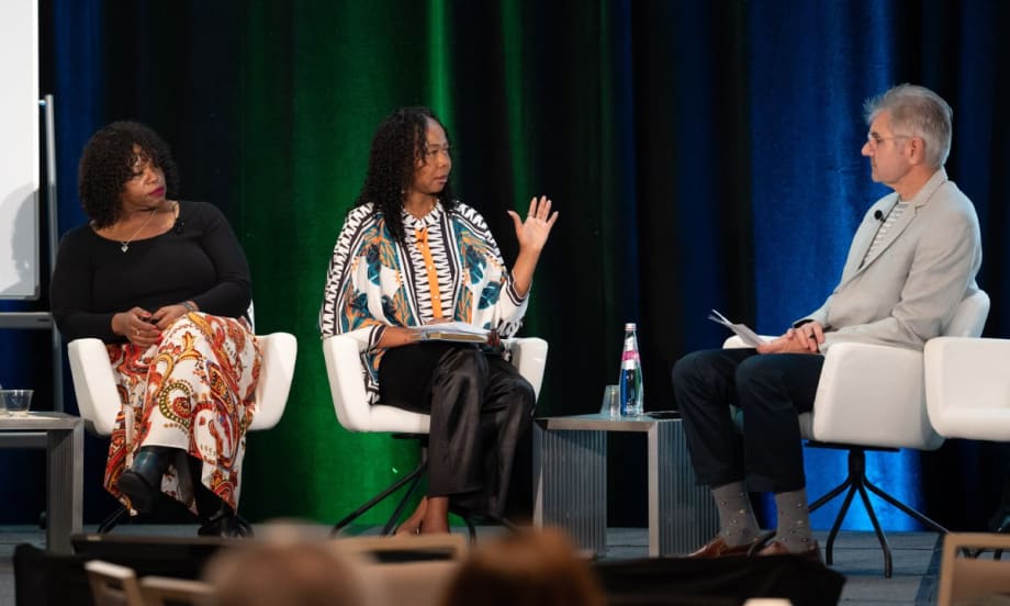 Two women and a man sit and talk on a stage.