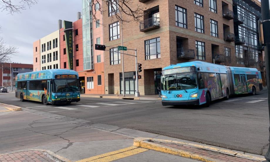 Two ABQ RIDE busses at an intersection by Gold street in front of a parking structure.