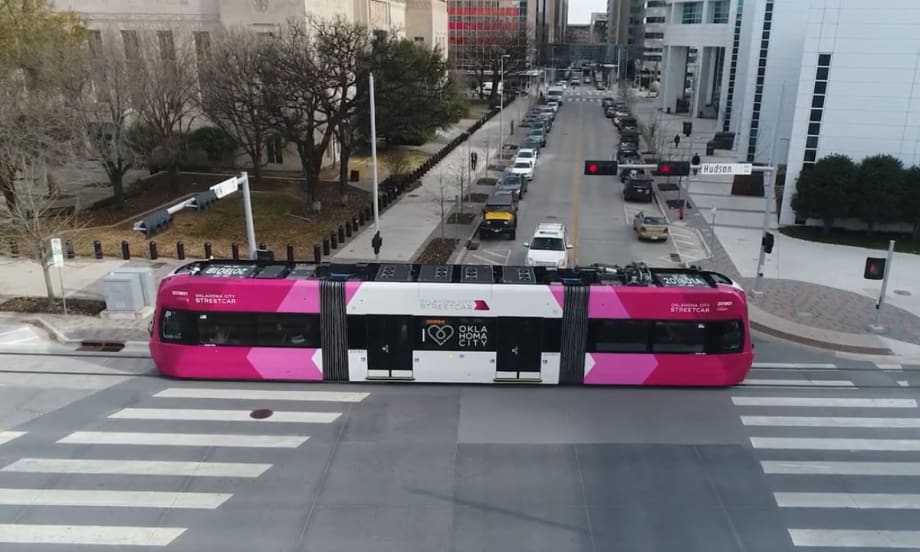 An pink and white OKC streetcar moves down a street.