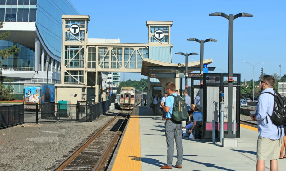 Commuter rail riders wait on a station platform.
