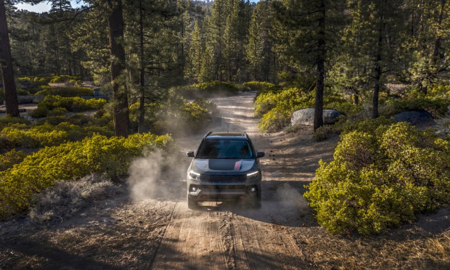 A photo of the 2026 Jeep Compass driving on a dirt road through the woods.