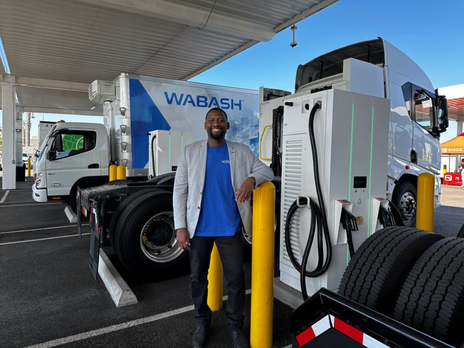 Man stands in electric truck charging depot.