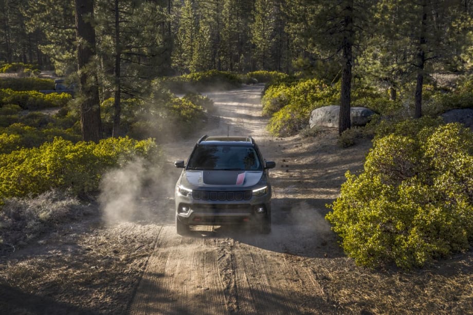A 2025 Jeep Compass Trailhawk driving on a dirt road in a forest.
