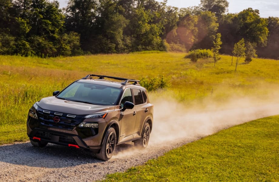A tan SUV drives down a dirt road.