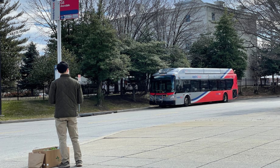 A rider waits for a WMATA bus on a sidewalk.