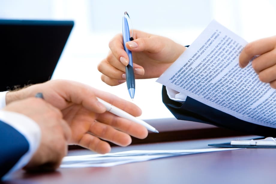 Two sets of hands holding pens and paper over a table during a business meeting.
