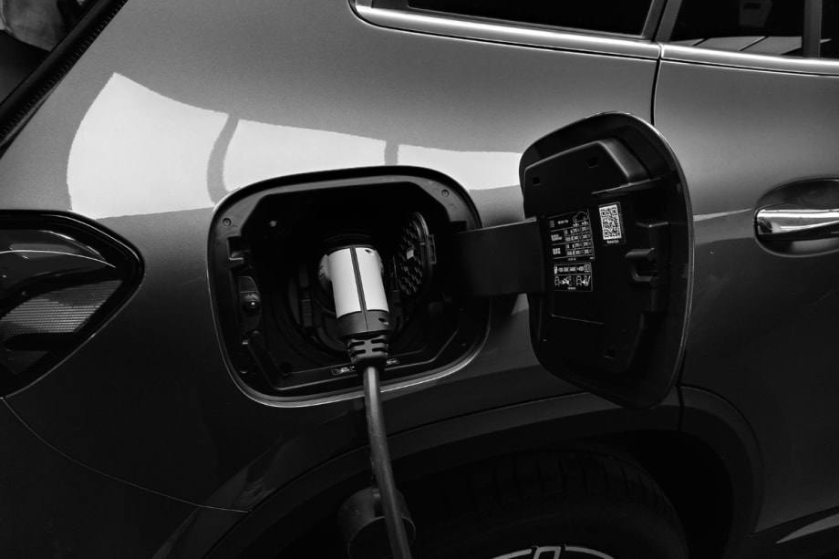 The open charging port of a gray electric vehicle with a charging cable attached.