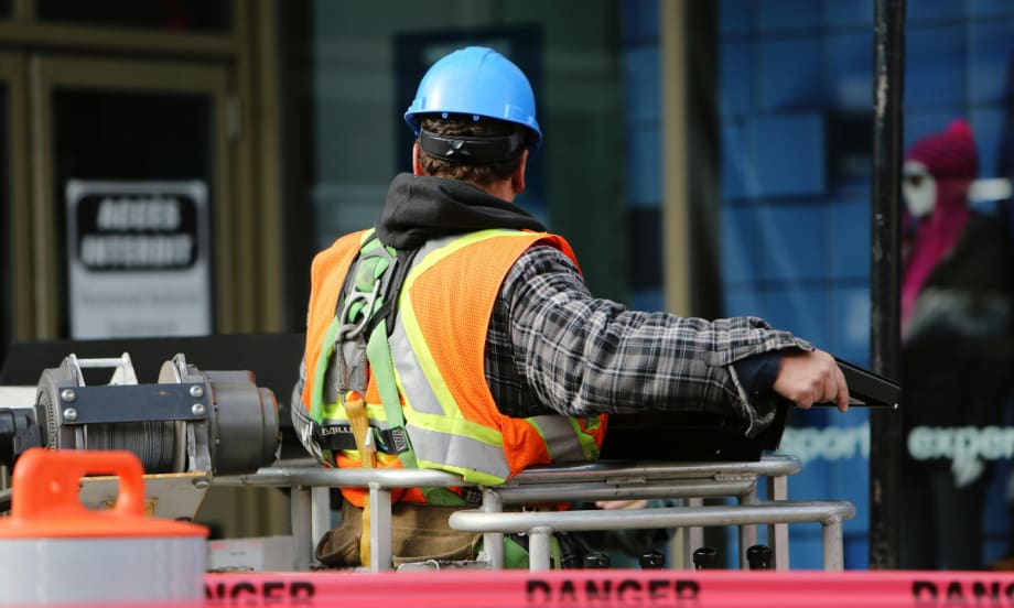 The back of a construction worker wearing a blue hard hat and an orange visibility vest.