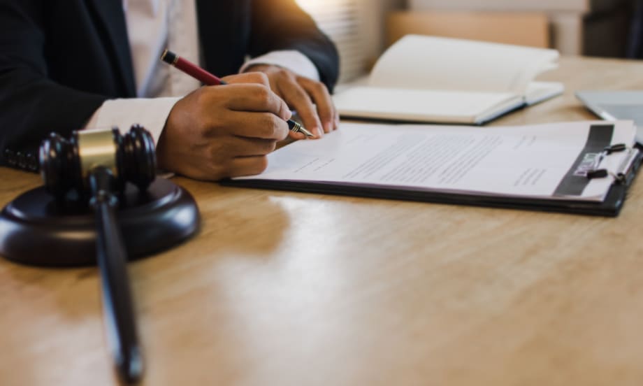 hand signing paperwork on a clipboard on top of a desk with a gavel to the side