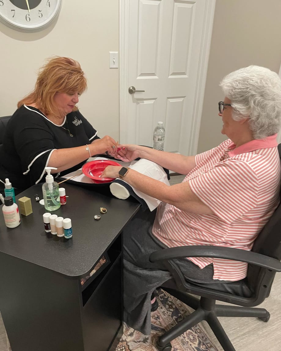Two women face each other over a manicure table, as one woman gives the other woman a manicure.