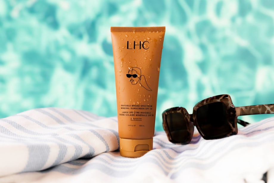 a bottle of LHC sunscreen on a towel next to a pair of sunglasses