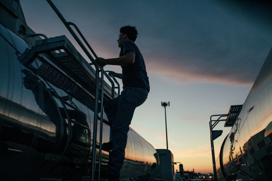 Truck driver climbs side of tanker trailer at sunset or sunrise