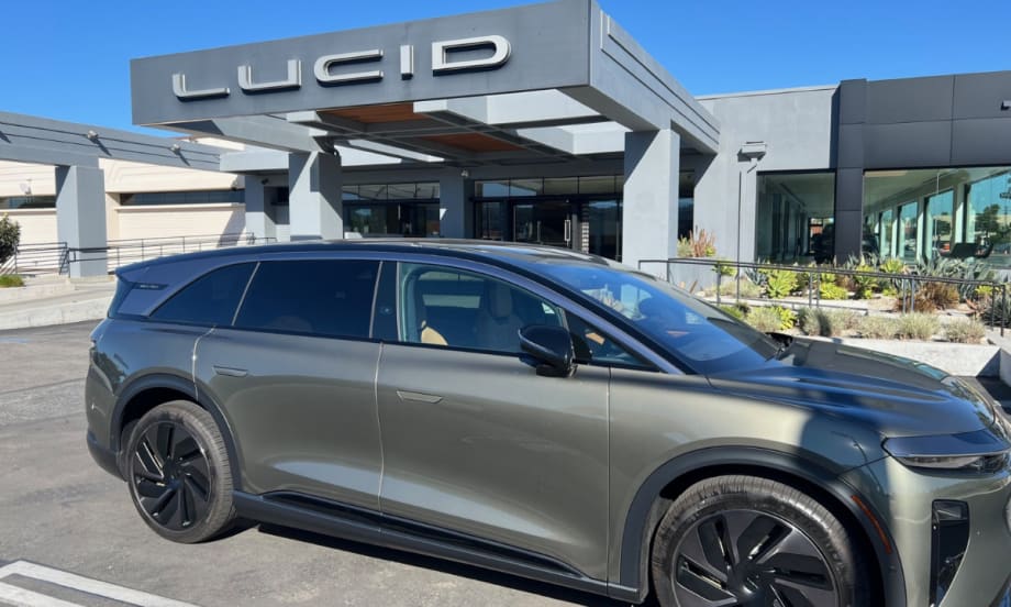 A right-side view of a gray Lucid Gravity Grand Touring in front of a Lucid dealership entrance.