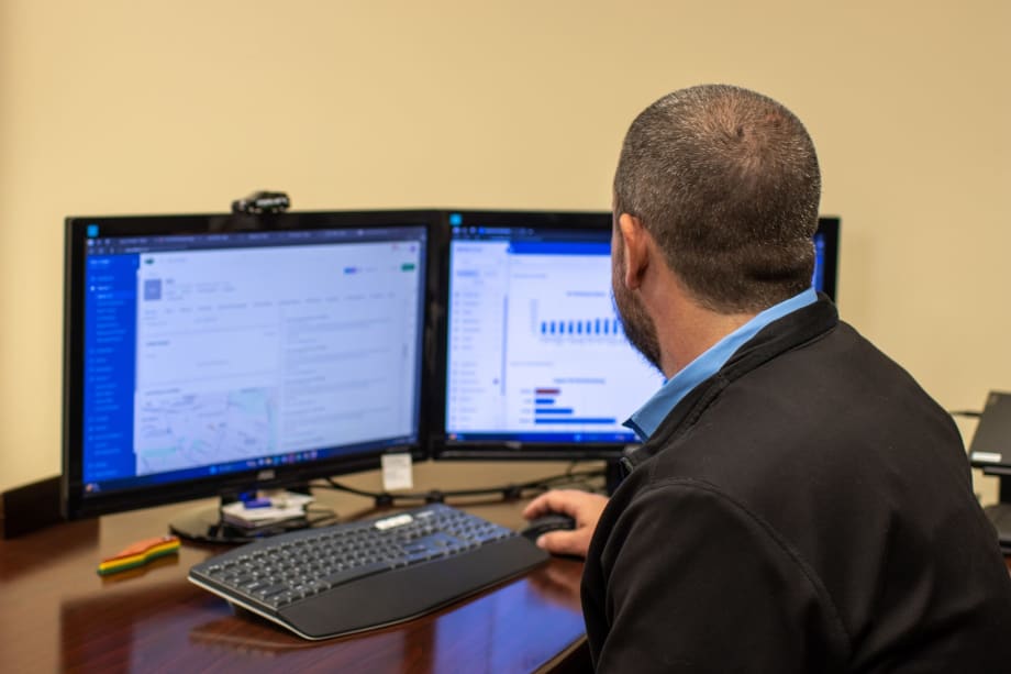 Fleet manager reviews maintenance and performance data on dual computer monitors.