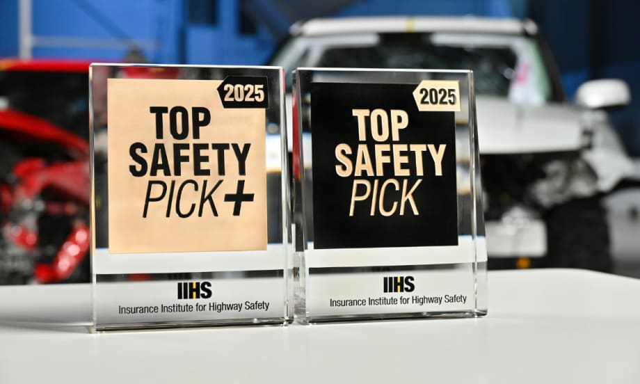 Close up image of Top Safety Pick+ and Top Safety Pick awards in front of crash test cars.