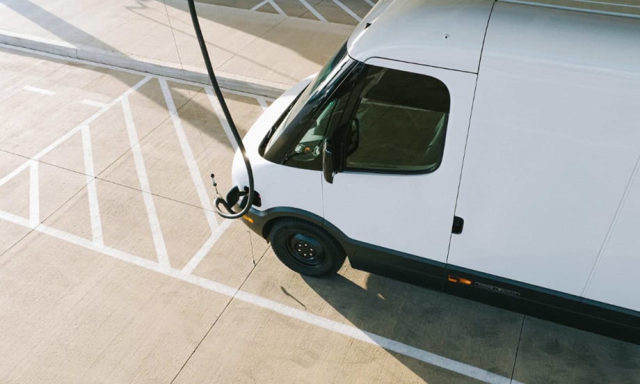 A white Rivian commercial van is charging in a parking lot.