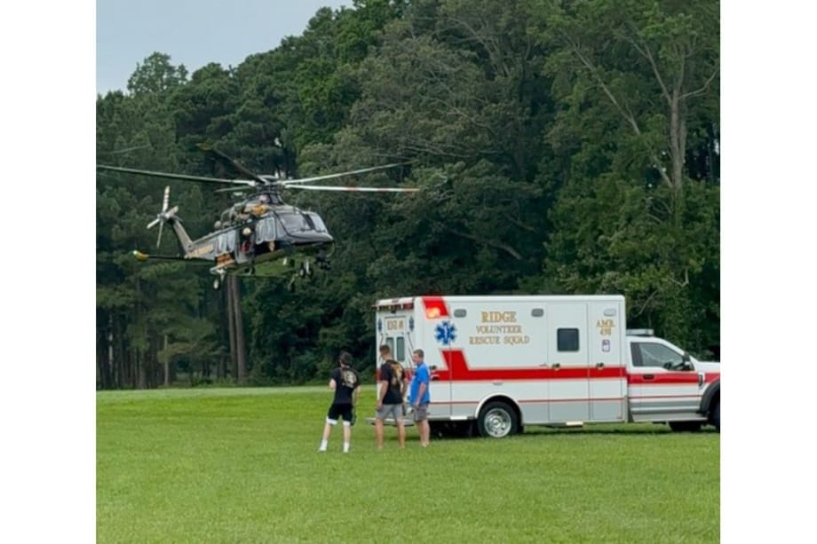 Medical helicopter landed on grassy field near ambulance with people nearby