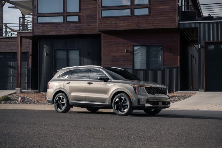 A tan and black Kia SUV parked on the street in front of a modernized brick house.