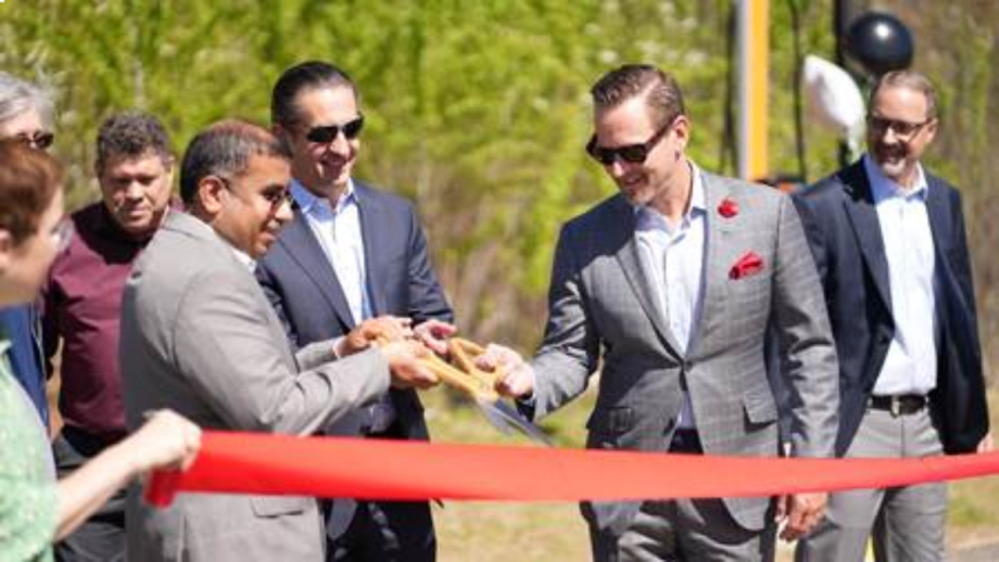 Three men in suits cut a red ribbon at an outdoor opening ceremony.