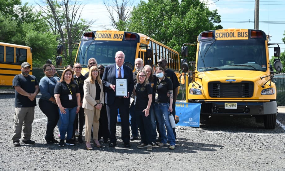 A group poses with two Thomas Built Buses Safe-T-Liner C2 Jouley electric school buses parked outside.