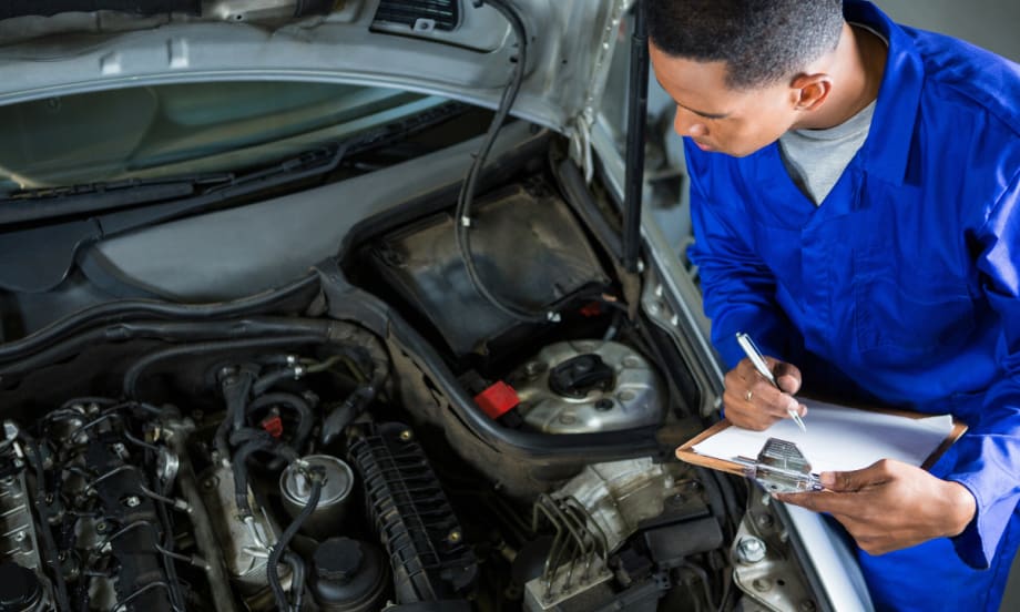 mechanic filling out clipboard while inspecting under hood of vehicle