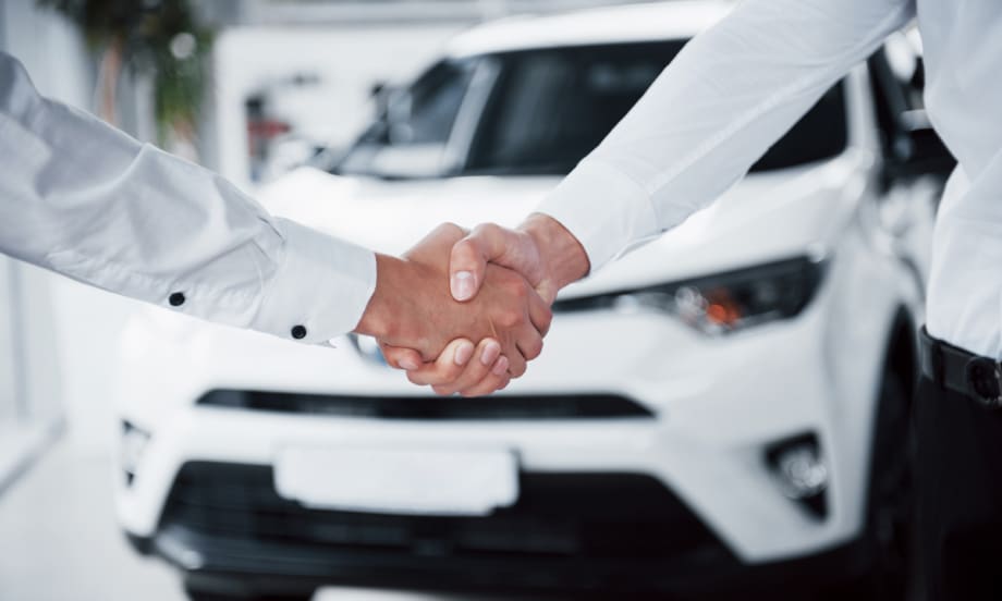 two people shaking hands in front of a new car that says Smarter Deals Ahead