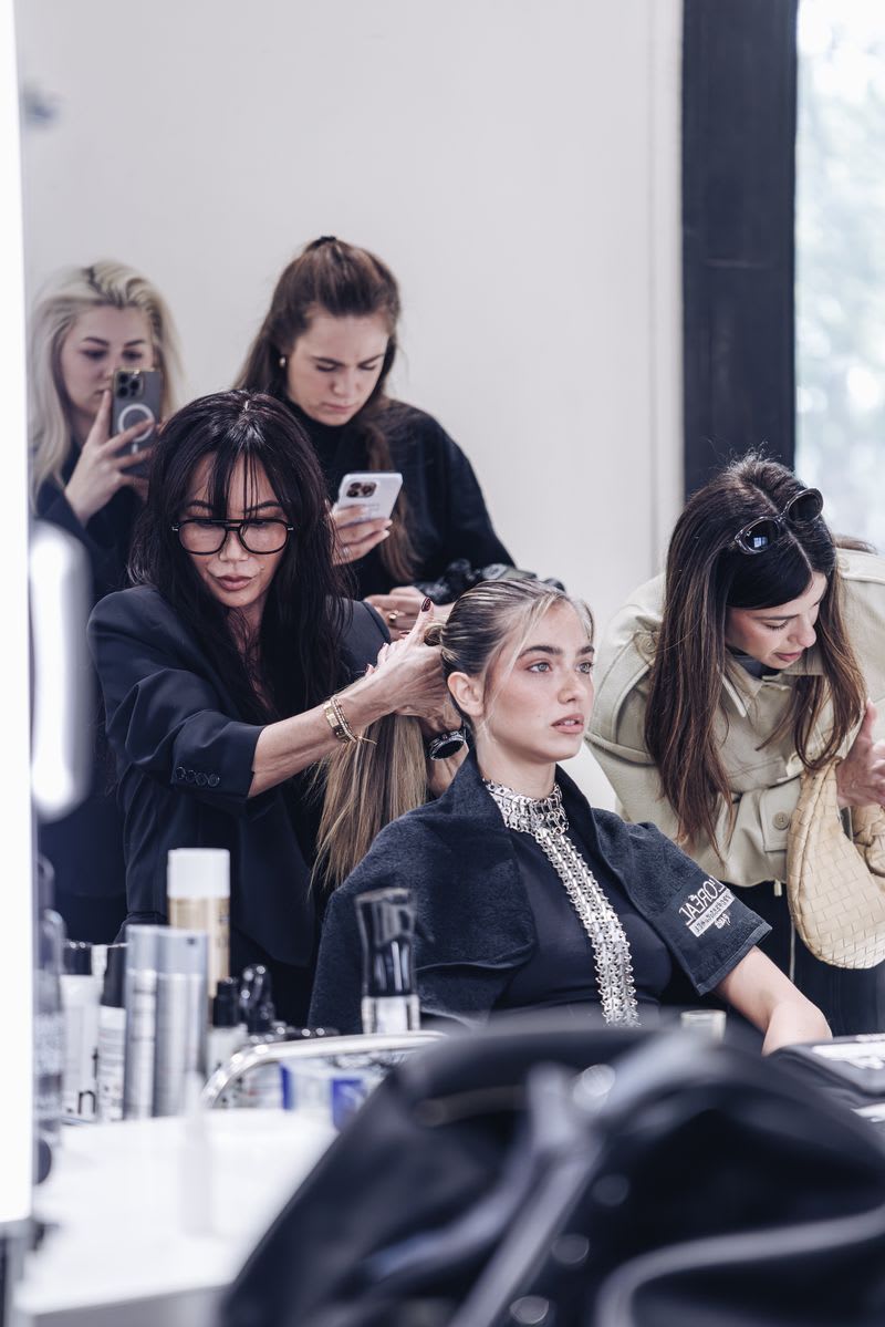 A stylist pulls a model's hair into a ponytail as influencers snap pictures with their iphones