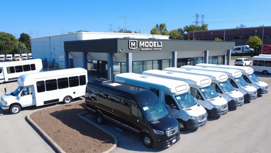 Model 1 Commercial Vehicles facility in Elgin, Illinois with a lineup of commercial vans and shuttle buses parked outside the dealership and service center supporting fleet customers in the Chicago area.