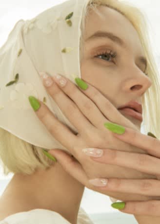 A young woman with blonde hair, a head scarf, and green nails.