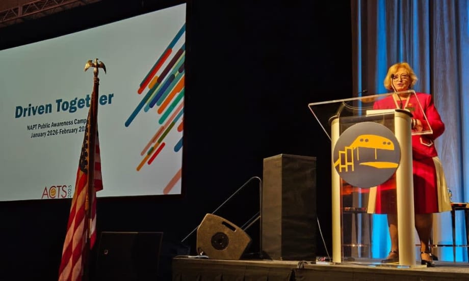 Molly McGee Hewitt stands at a podium on a stage with a screen behind her that says "Driven Together" and the NAPT logo
