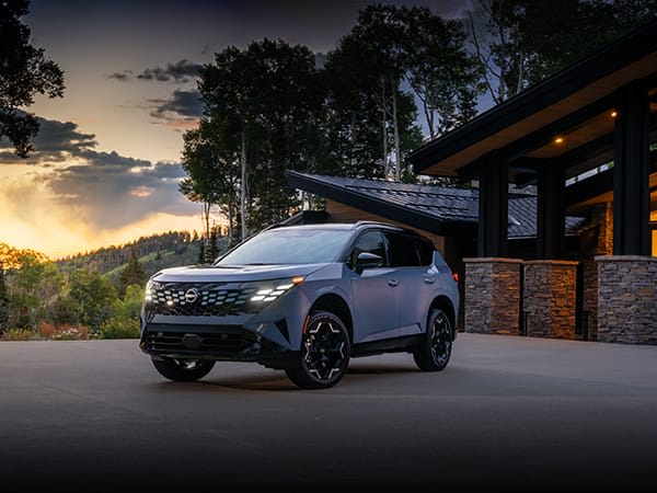 A grey Nissan drives on a road at sunset