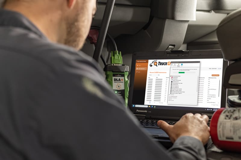 Technician using Truck Check-Up diagnostic software on a Panasonic Toughbook laptop inside a truck cab