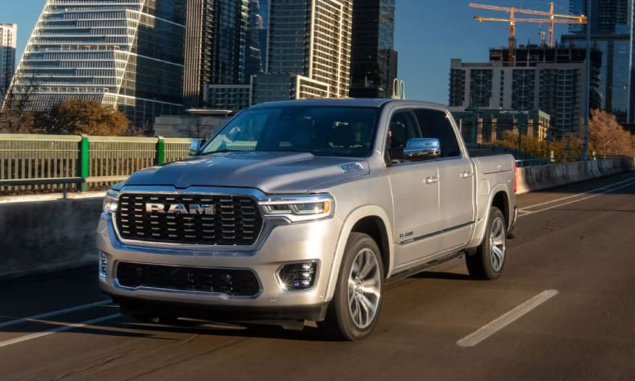 An image of a silver 2025 Ram 1500 pickup truck driving on a city road with skyscrapers and construction in the background.