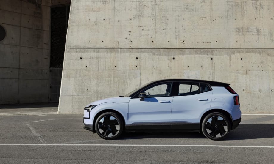 The left side view of a cloud blue 2025 Volvo EX30 parking in front of a gray concreate wall.