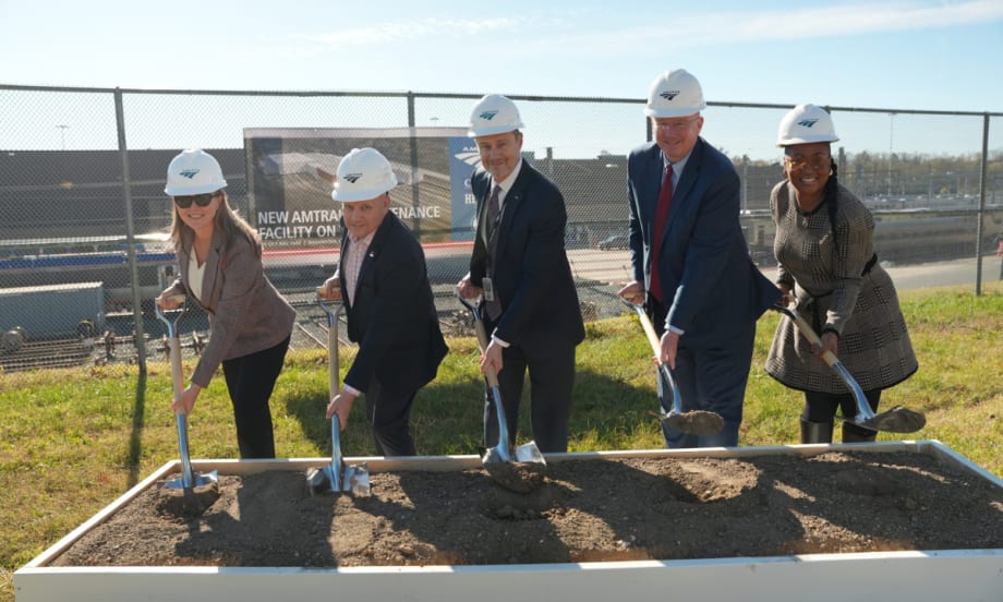 Five people in business attire lined up shoveling dirt.
