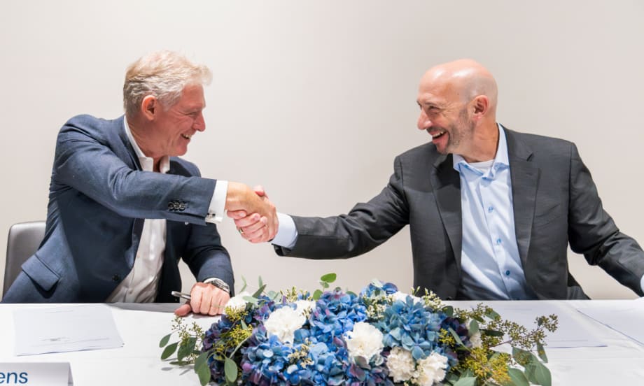 Tim Albertsen and Shlomo Crandus shake hands at a table with a blue flower bouquet on it.