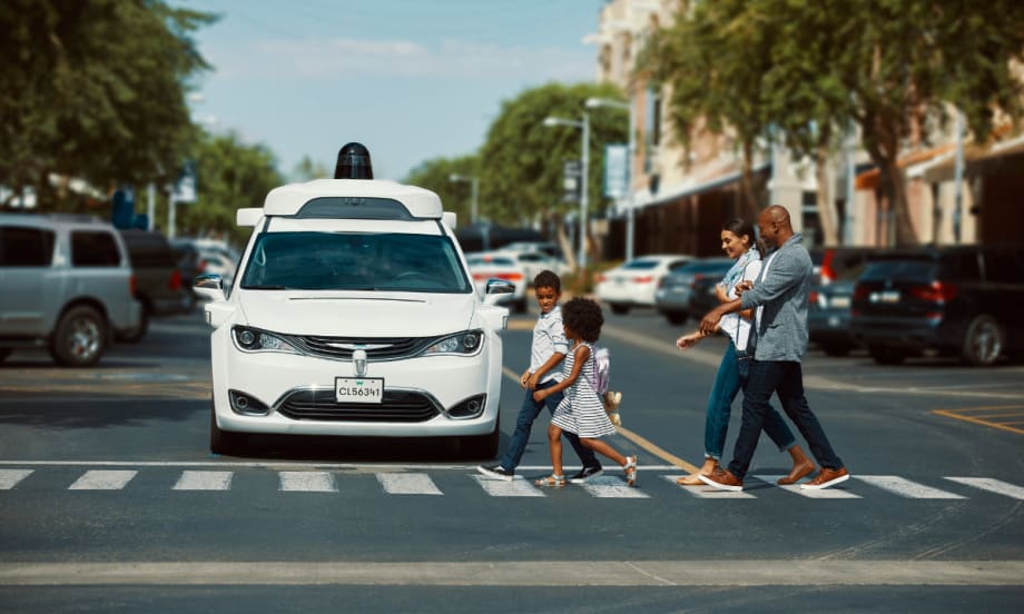 A white Waymo vehicle waits at a crosswalk as a family crosses.
