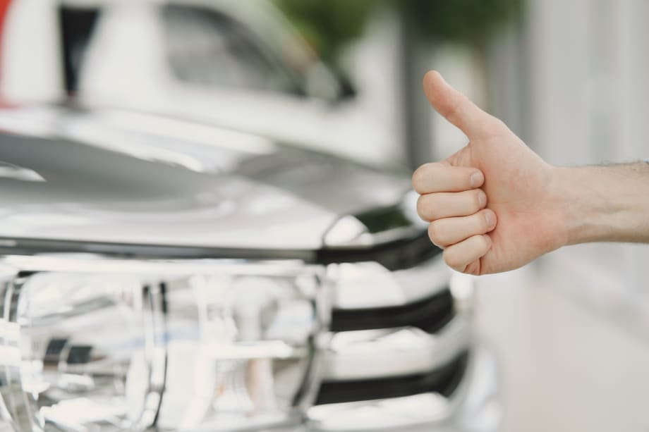 car in background with hand giving a thumbs up in front