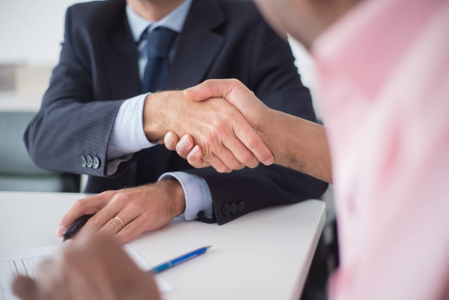 Photo of a man in a suit shaking hands with a man across a desk