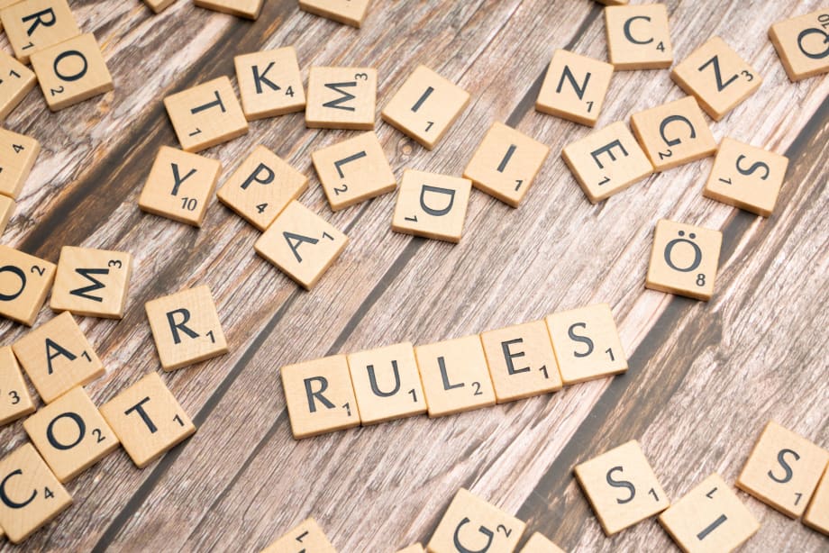 Scrabble tiles  spelling out 'Rules' among random letter tiles, all on a wooden surface