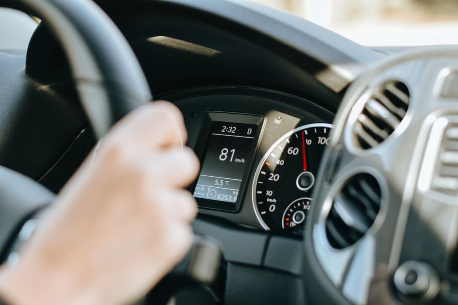 Photo of a woman's hand gripping a steering wheel with the dashboard display in the background