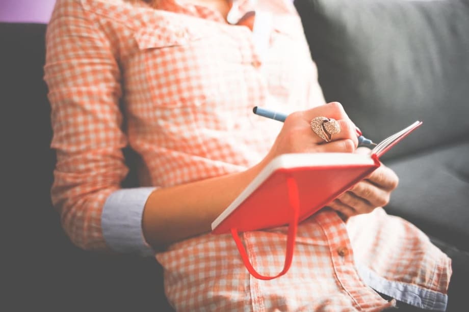 The torso of a woman, writing in a book.