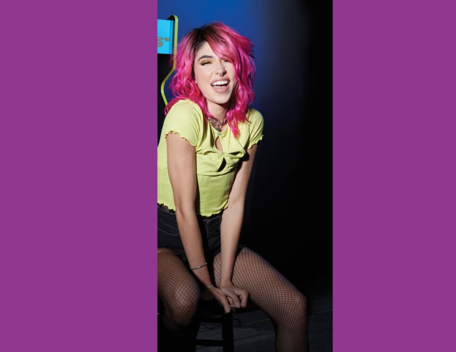 a woman with pink hair and a green shirt sitting and smiling
