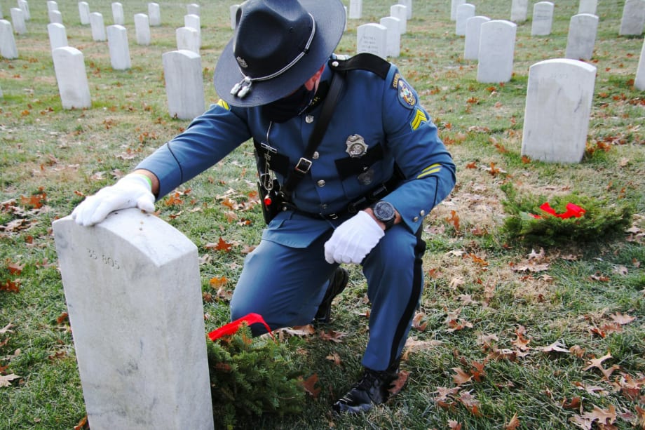 A state trooper takes a moment beside a veteran’s headstone at Arlington National Cemetery.[|CREDIT|]PHOTO: Wreaths Across America