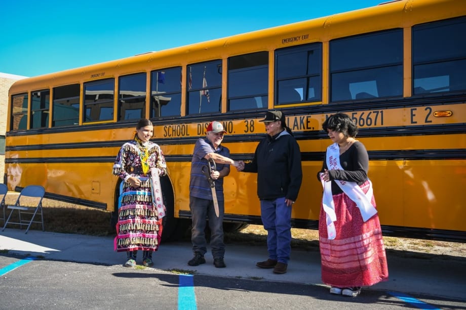 three people cut a ribbon in front of a school bus